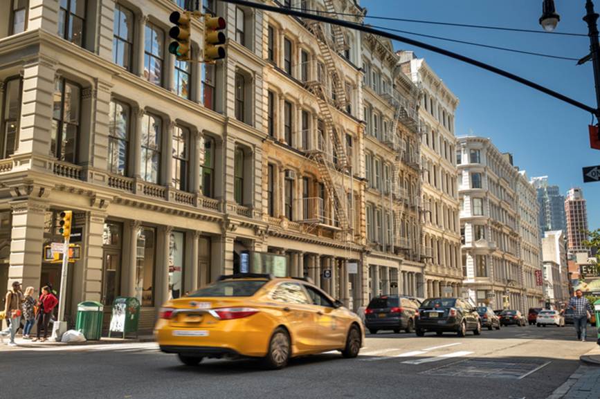 Street view of a yellow taxi cab driving in New York City. 